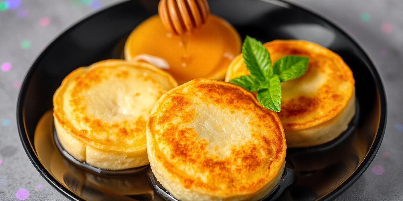 Golden pancakes being drizzled with honey, served with fresh mint.