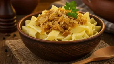Traditional Hungarian dish called Káposztás tészta, served in a rustic ceramic bowl on a wooden table.