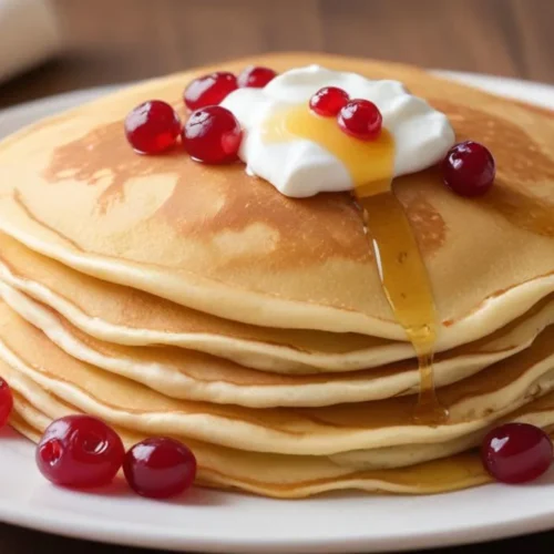 A stack of thin Swedish pannkakor pancakes topped with lingonberry jam and powdered sugar on a white plate.