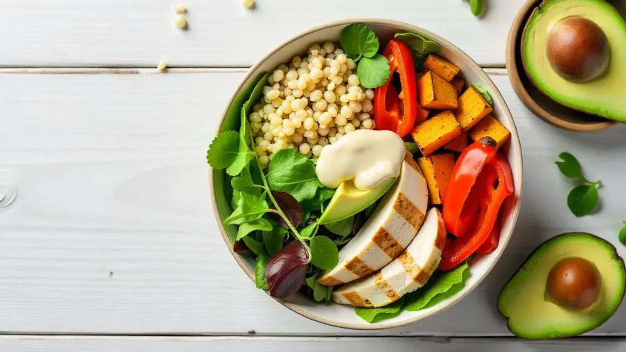 Colorful protein bowl with grilled chicken, quinoa, greens, avocado, bell peppers, and sweet potatoes.