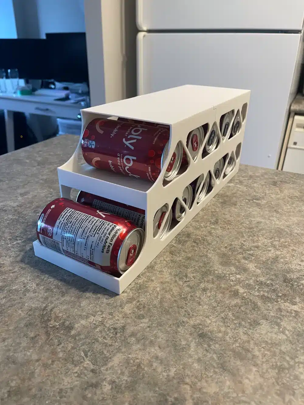 White 3D printed can dispenser holding red soda cans on a kitchen counter, designed for efficient storage and easy access in the fridge or pantry