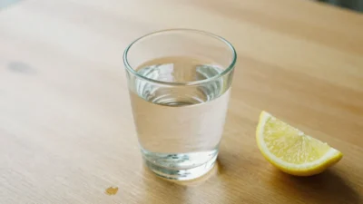 A nearly empty glass of water with soft natural light and a lemon slice on a wooden surface, symbolizing the risks of dehydration.